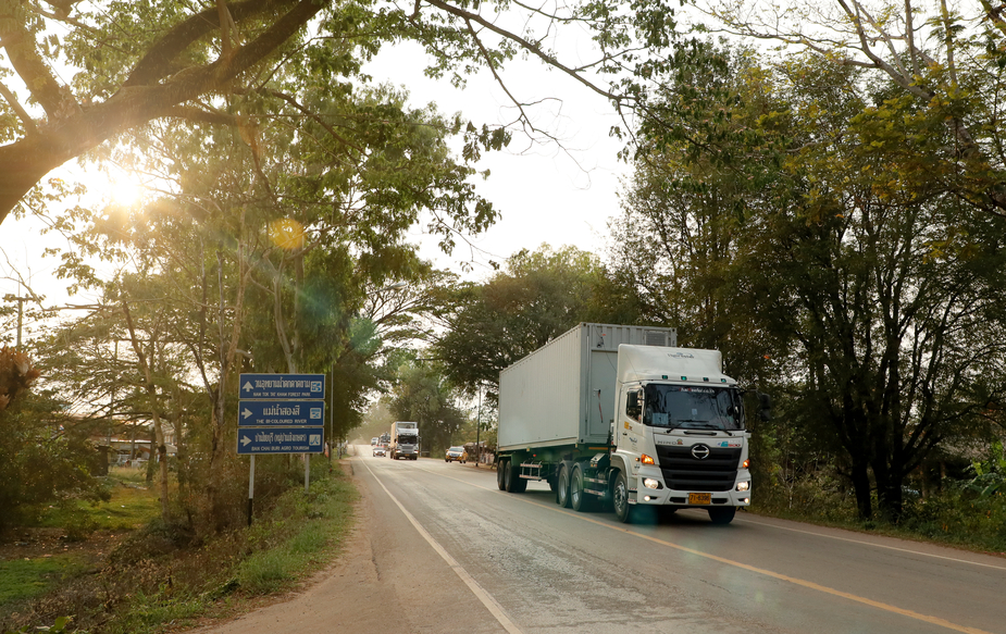 A large white container truck, part of the extensive logistics for international production services in Asia, drives down a highway in rural Thailand during a location move.